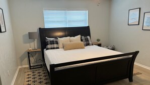 Ein Schlafzimmer mit Bett, Nachttisch, Lampe, einem Fenster mit Jalousien und einem Deckenventilator.