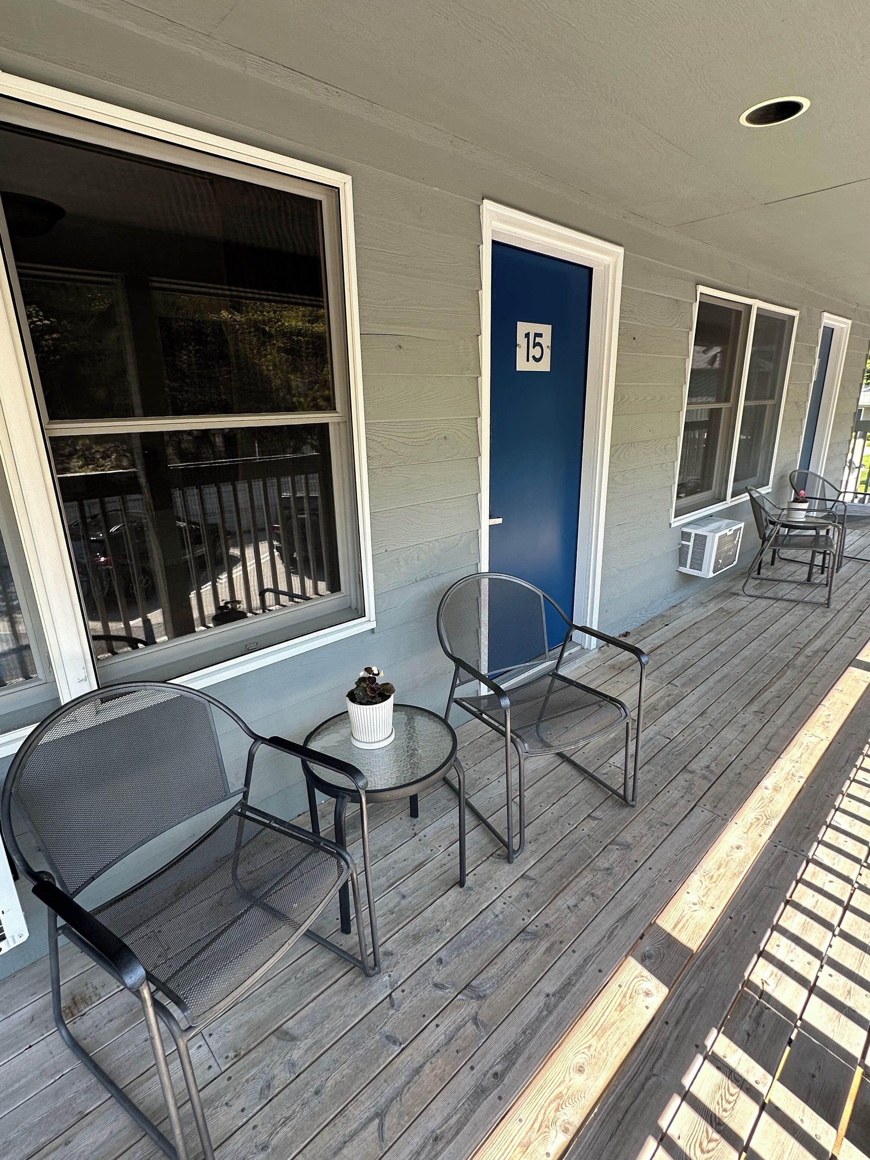 A covered porch with outdoor seating, a door marked with the number 15, and a small table with a potted plant.