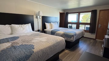 Et hotelværelse med to senge, et natbord, en lampe, et vindue med gardiner og en dør.