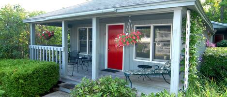 A house with a porch, a red door, and a garden with various plants and flowers.