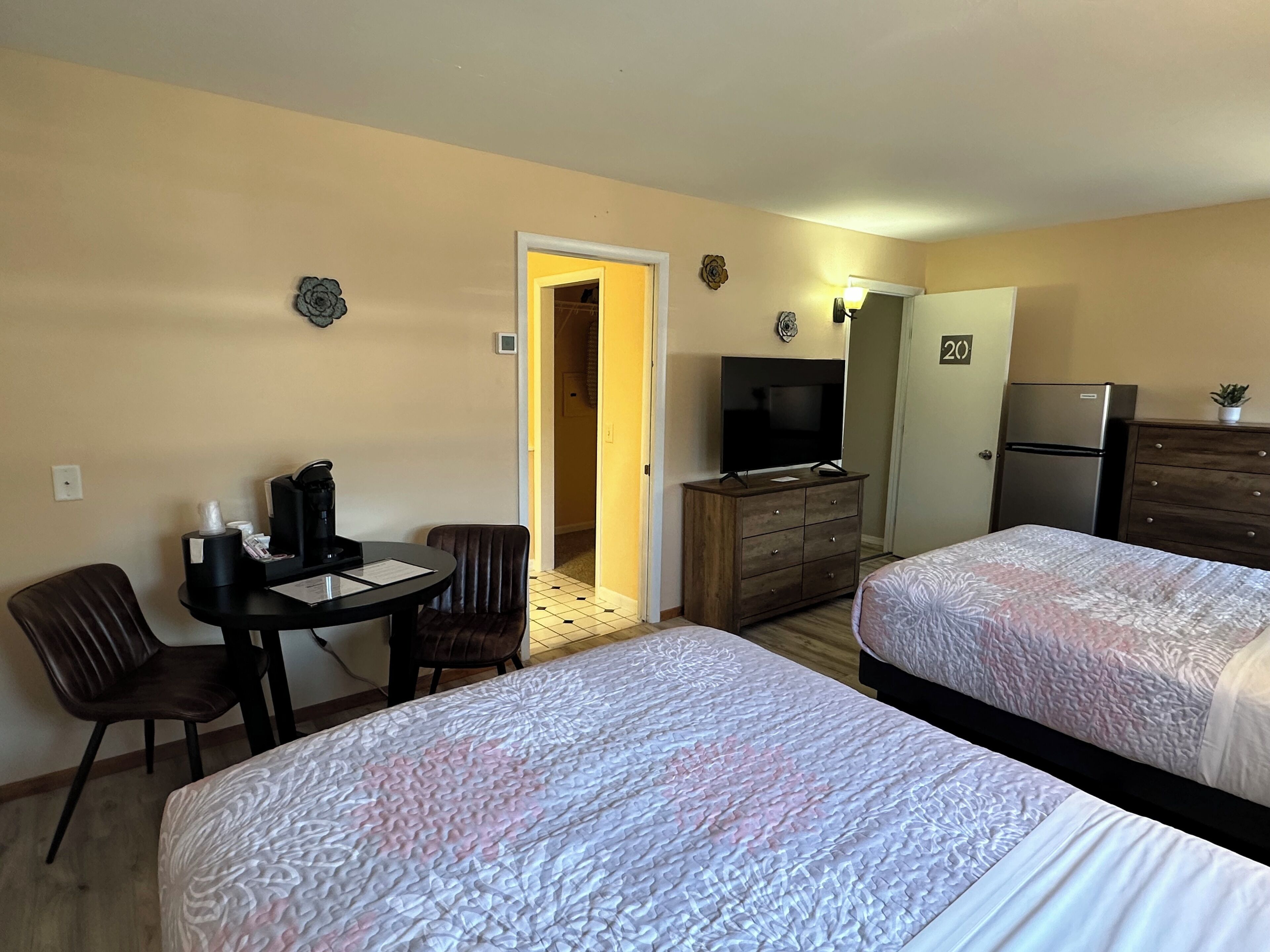 Ein Hotelzimmer mit zwei Betten, einem Fernseher, einem Kühlschrank, einem hölzernen Schminktisch, einem Schreibtisch mit Stuhl und einem kleinen Tisch mit Kaffeemaschine.