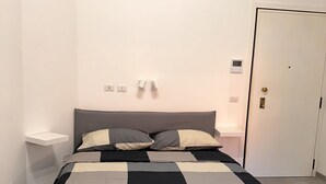 Una cama bien tendida con colcha a cuadros, una mesita de noche con lámpara y una puerta con cerradura.