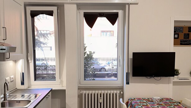 Una cocina funcional con ventana, una mesa de comedor con mantel colorido y un televisor de pantalla plana en la pared.