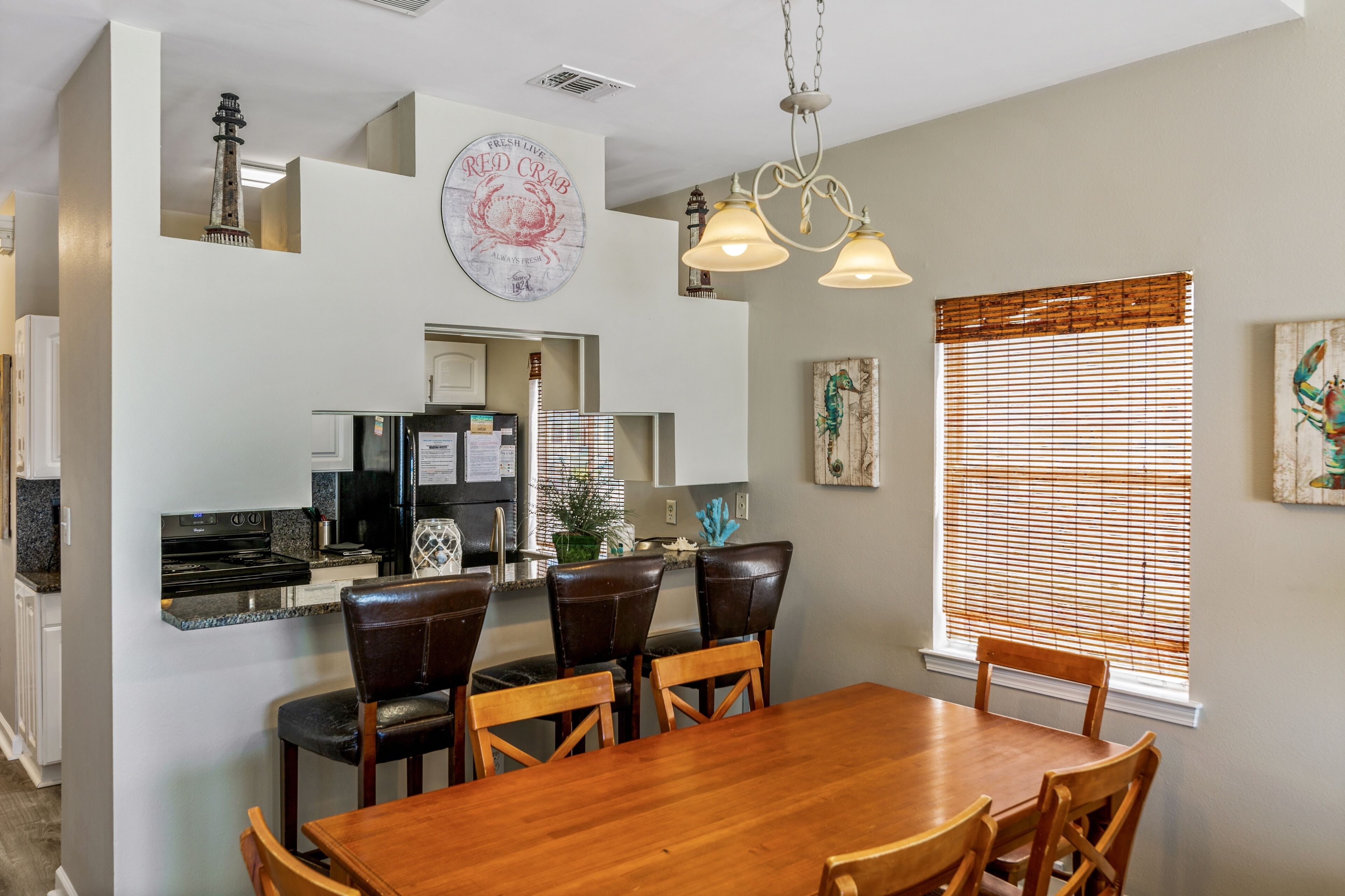 A dining area with a wooden table and chairs, a kitchen with a refrigerator and stove, and artwork on the walls.
