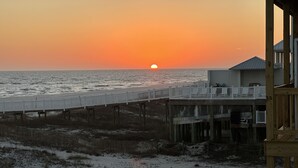 A beach view with a wooden pier extending into the ocean, a sandy beach, and a building with a balcony. - Gulf Shores Duplex Beachfront Pool -4bd  (Gulf Shores)