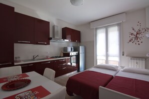 A compact hotel room with a kitchenette, a dining area, and a bed with two pillows.