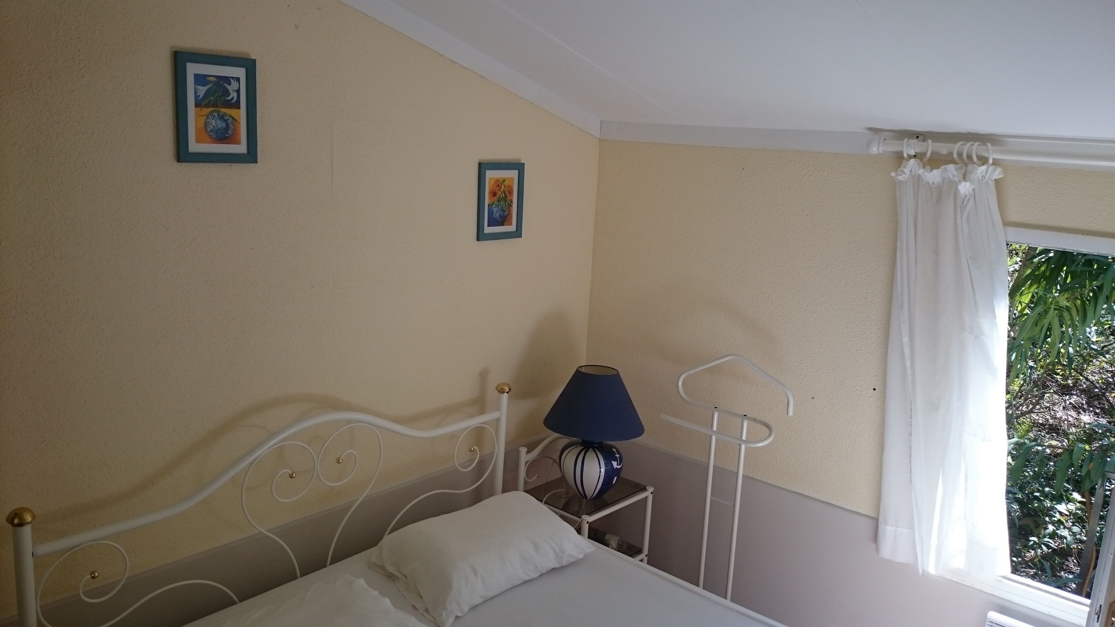 Un dormitorio con una cama, una mesita de noche con lámpara y dos cuadros en la pared.