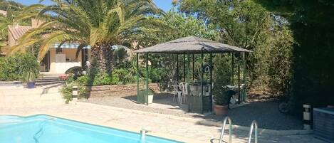 A pool area with a gazebo, palm trees, and a stone wall.