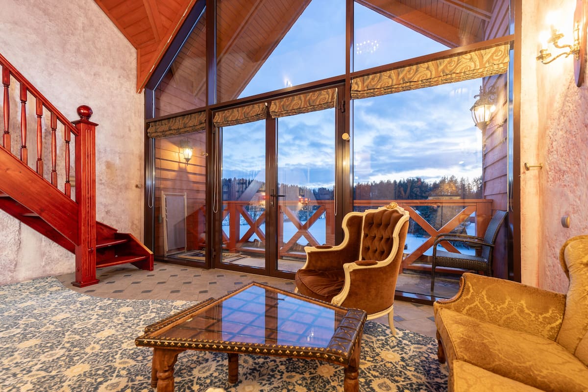 A spacious room with a large glass door leading to a balcony, a wooden staircase, and a plush armchair.
