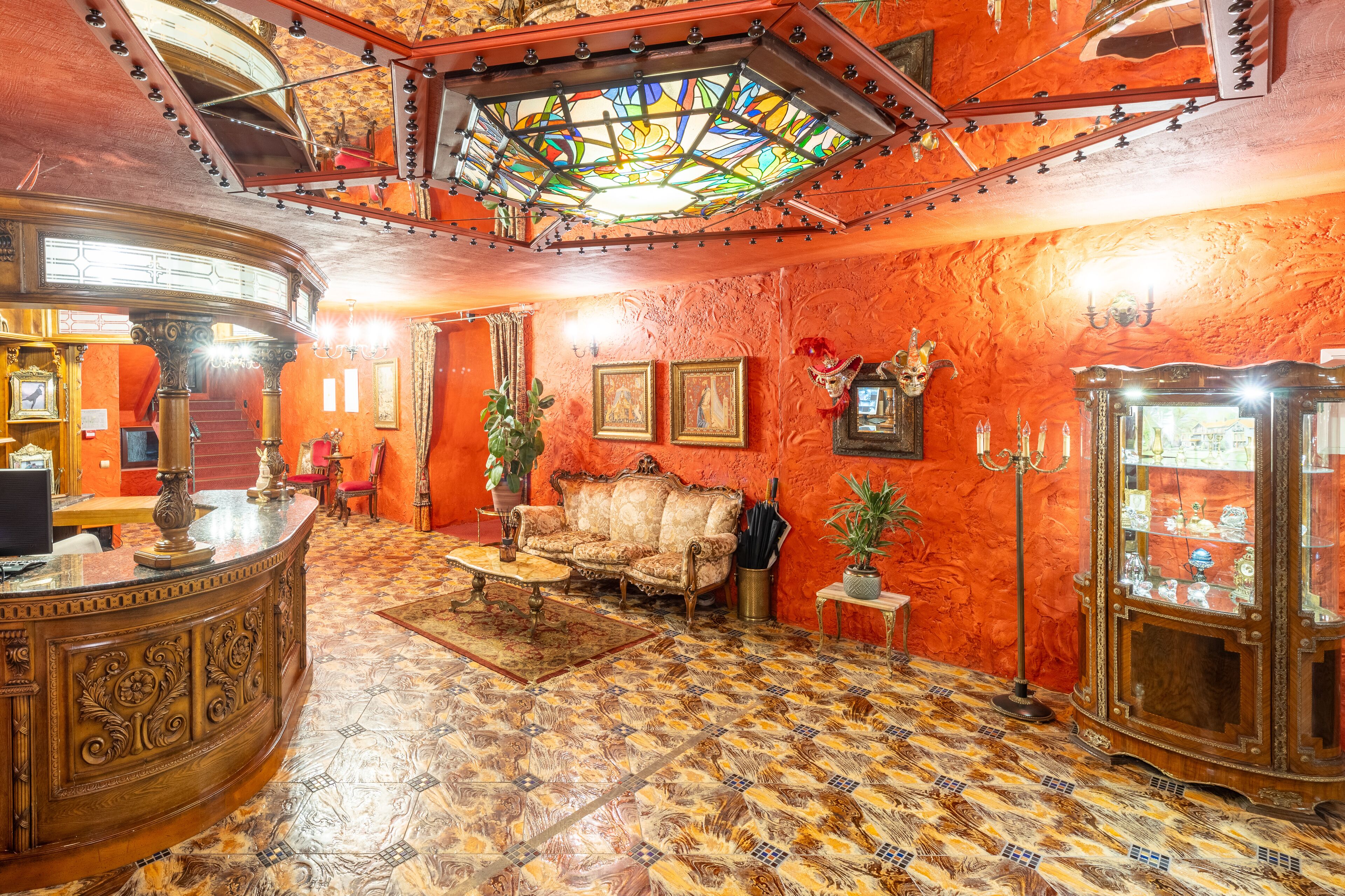 A room with a curved wooden reception desk, a vintage sofa, a patterned floor, and a stained glass ceiling.