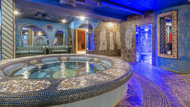 Een luxueus wellnessgedeelte met een groot rond bubbelbad, stenen muren en blauwe verlichting.