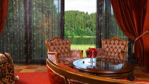 Een kamer met twee fauteuils, een ronde houten tafel en uitzicht op een meer door dunne gordijnen.
