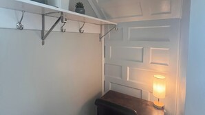 A small room with a white wall, a wooden bench, a table with a lamp, and a shelf with plants. - Cozy Condo in Downtown Roanoke VA 
 (Roanoke)