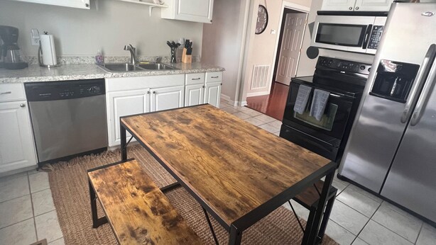 A modern kitchen with white cabinets, a wooden dining table, a ceiling fan, and stainless steel appliances. - Cozy Condo in Downtown Roanoke VA 
 (Roanoke)