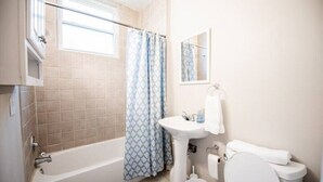 A bathroom with a bathtub, a sink, a toilet, and a window with a curtain. - Cozy Condo in Downtown Roanoke VA 
 (Roanoke)