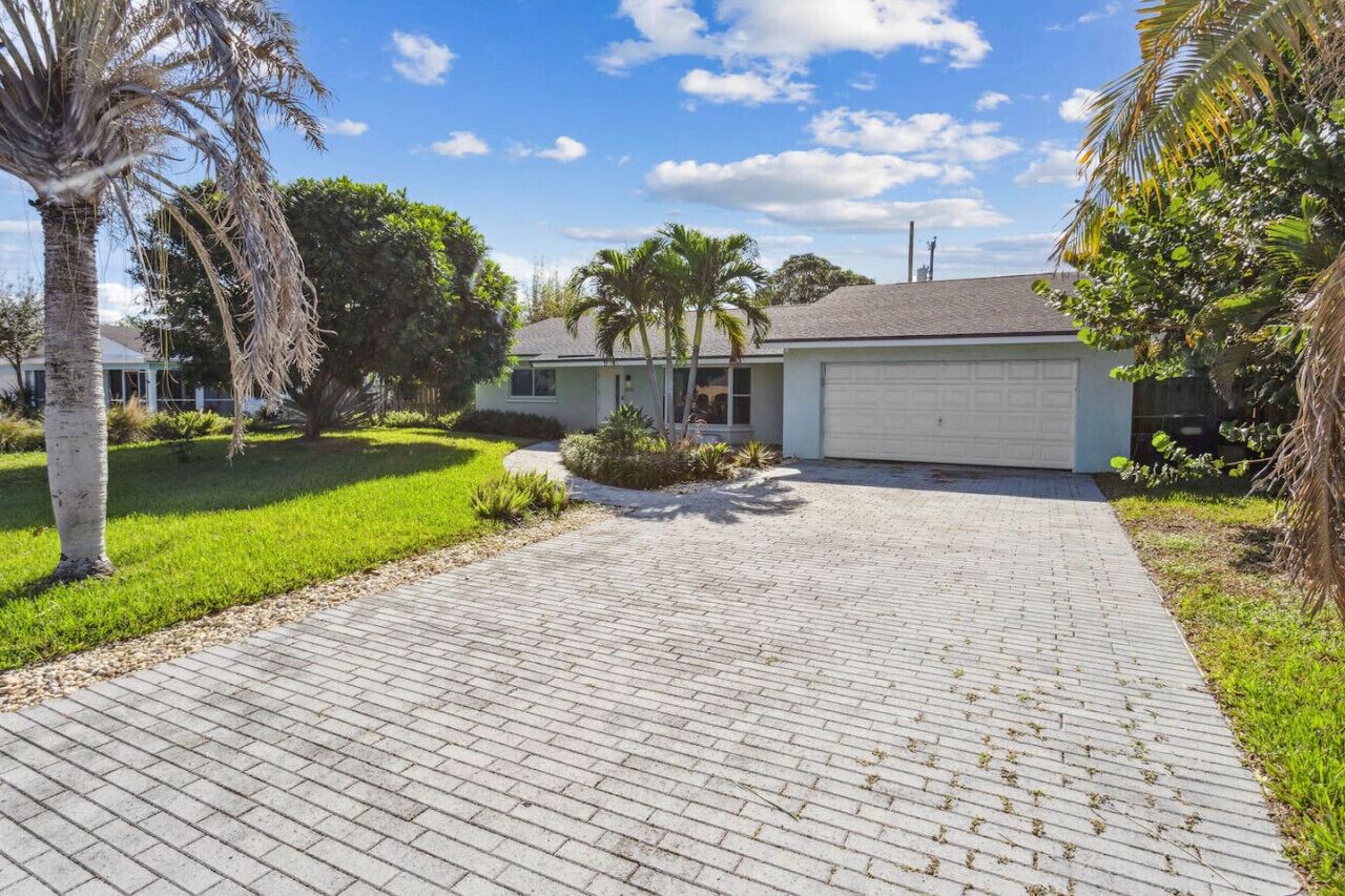A residential house with a paved driveway, palm trees, and a garage.