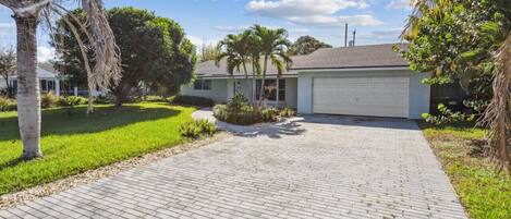 A residential house with a paved driveway, palm trees, and a garage.