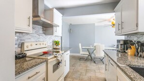 A modern kitchen with white cabinets, a marble backsplash, granite countertops, and a dining area with a glass table and chairs. - Beach Retreat Downtown Hot Tub (Delray Beach)