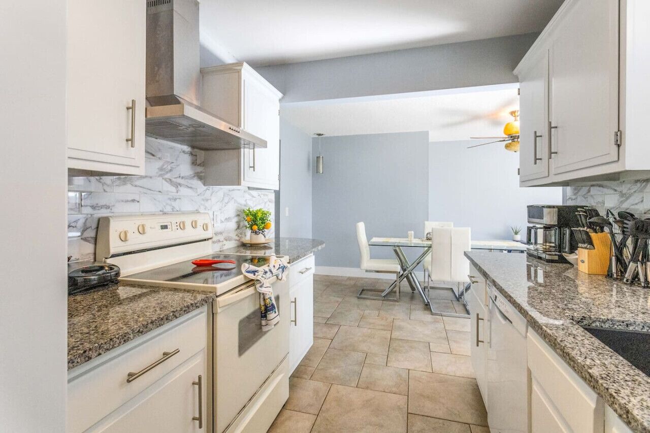 A modern kitchen with white cabinets, a marble backsplash, granite countertops, and a dining area with a glass table and chairs.