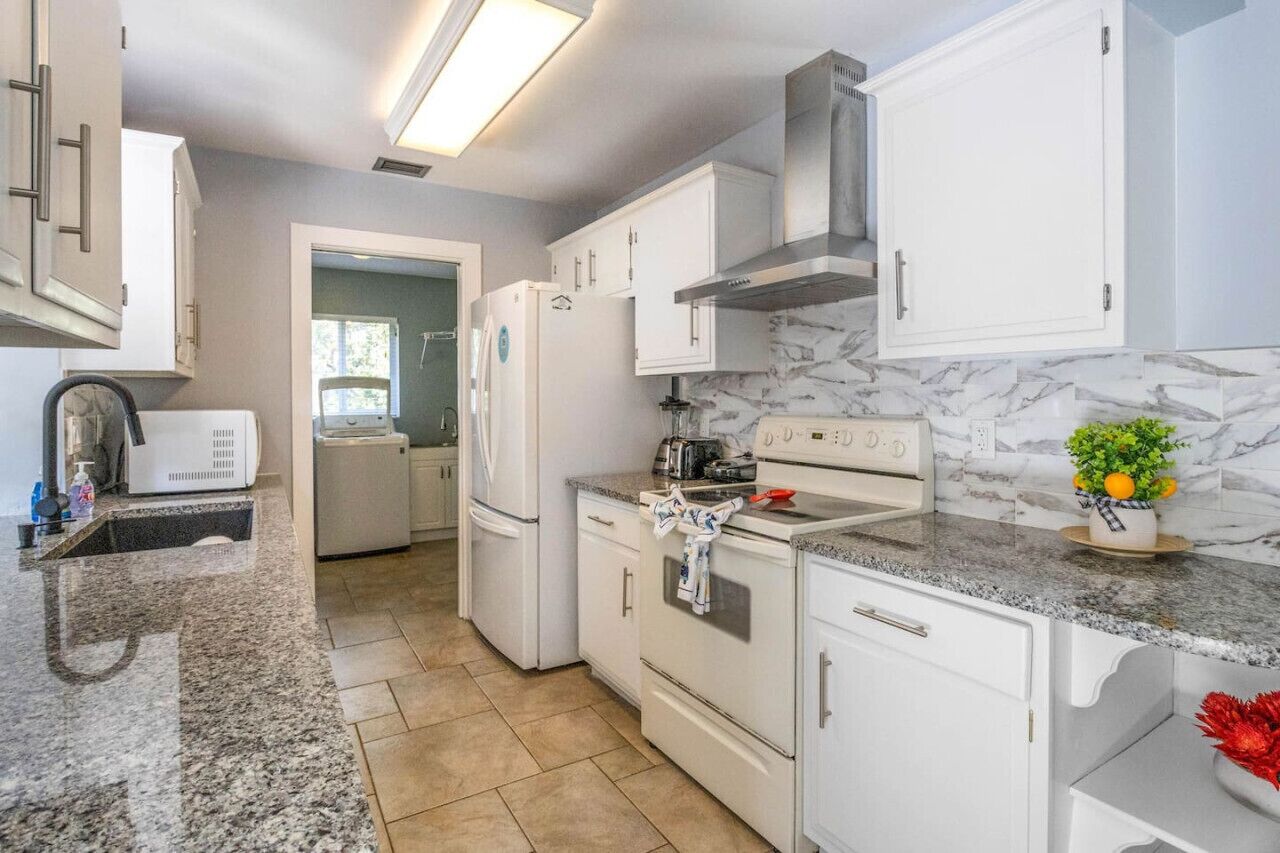 A modern kitchen with white cabinetry, a granite countertop, and a marble backsplash.
