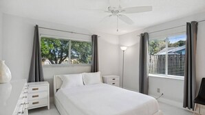 A bedroom with a bed, bedside tables, a lamp, and a window with curtains. - Beach Retreat Downtown Hot Tub (Delray Beach)