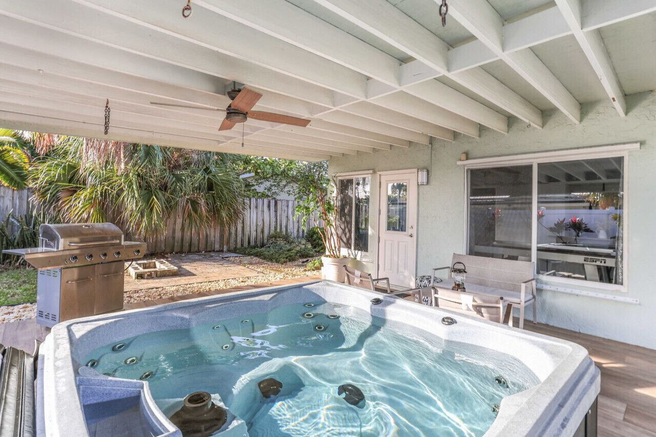A covered outdoor area with a hot tub, a ceiling fan, and a barbecue grill.