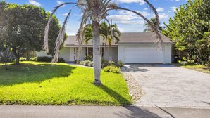A residential house with a well-maintained lawn, a palm tree, and a driveway leading to a garage. - Beach Retreat Downtown Hot Tub (Delray Beach)