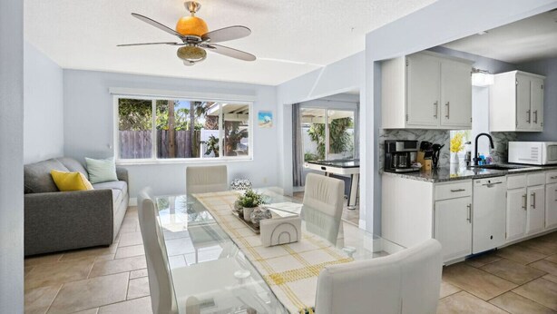 A modern kitchen with white cabinets, a dining area with a glass table, and a ceiling fan. - Beach Retreat Downtown Hot Tub (Delray Beach)