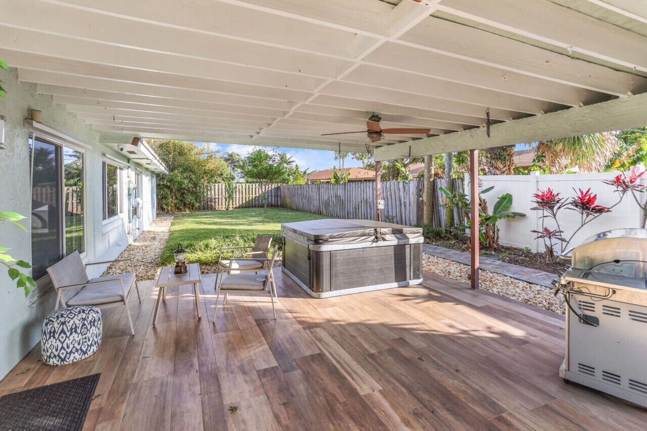 Un patio couvert avec une terrasse en bois, des meubles d’extérieur, un jacuzzi et un barbecue.