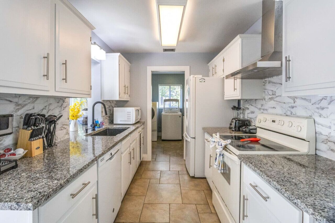 A modern kitchen with white cabinets, granite countertops, a microwave, a refrigerator, and a stove.