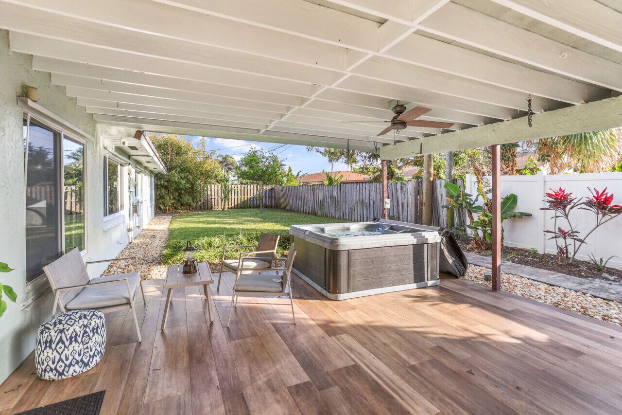 A covered patio with a hot tub, seating area, and a wooden deck.