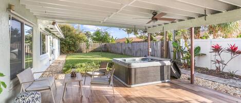 A covered patio with a hot tub, seating area, and a wooden deck.