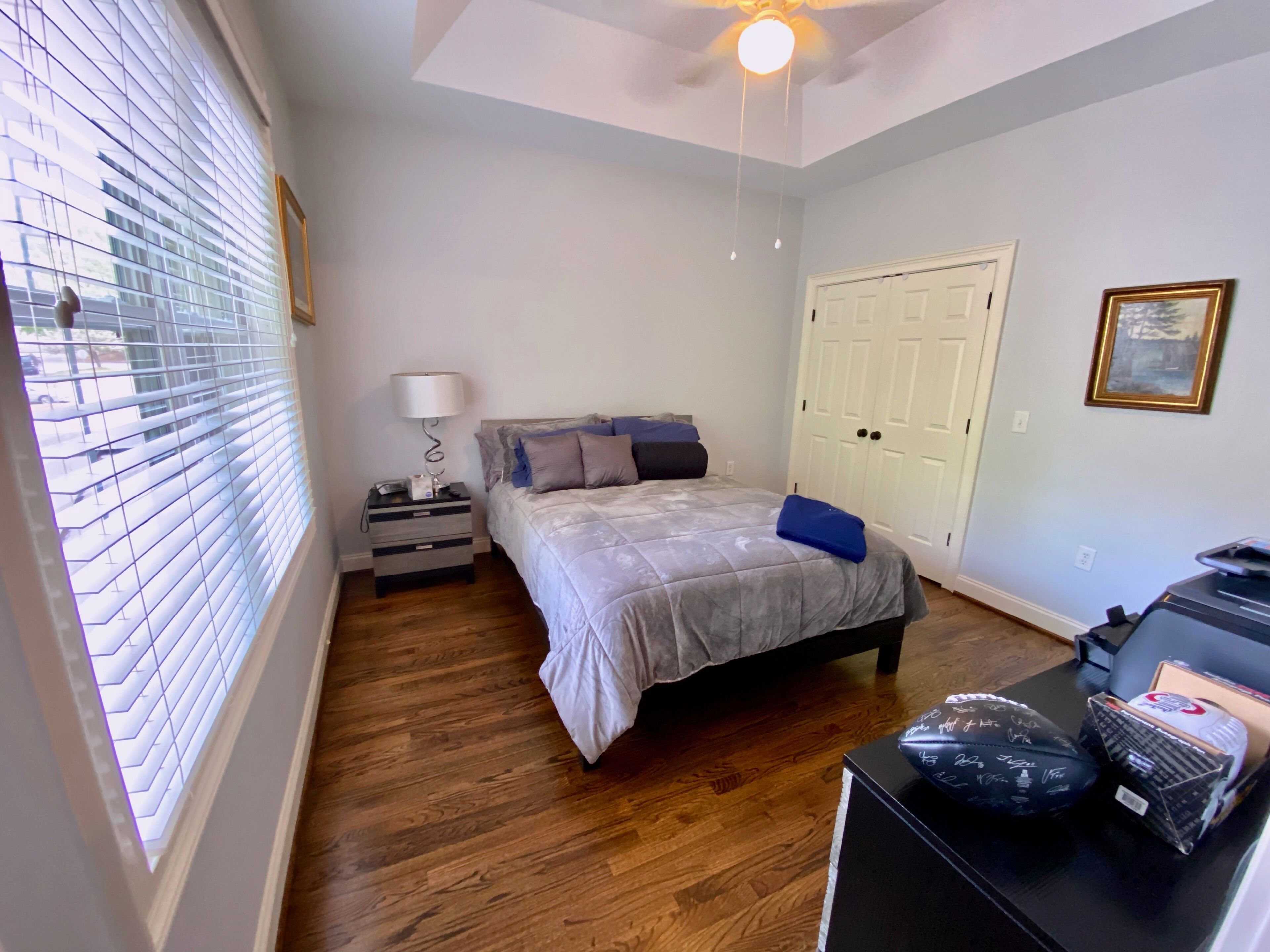 A bedroom with a bed, bedside table, lamp, and a desk with items on it.