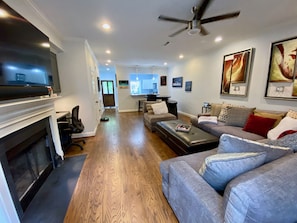 A spacious living room with a fireplace, a ceiling fan, and a large flat-screen TV.