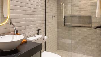 Un baño moderno con lavamanos blanco, inodoro y cabina de ducha con mampara de vidrio.