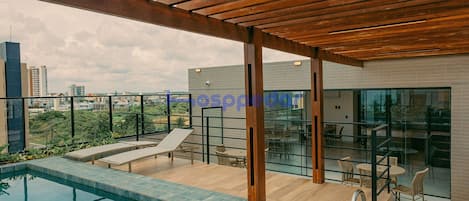 Piscina en la azotea con una pérgola de madera, sillas de descanso y barandilla de vidrio con vistas a la ciudad.