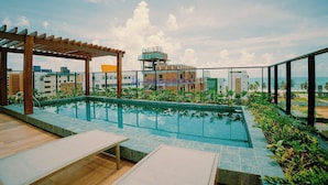 Una piscina en la azotea con sillas de descanso, una pérgola y vistas de la ciudad.