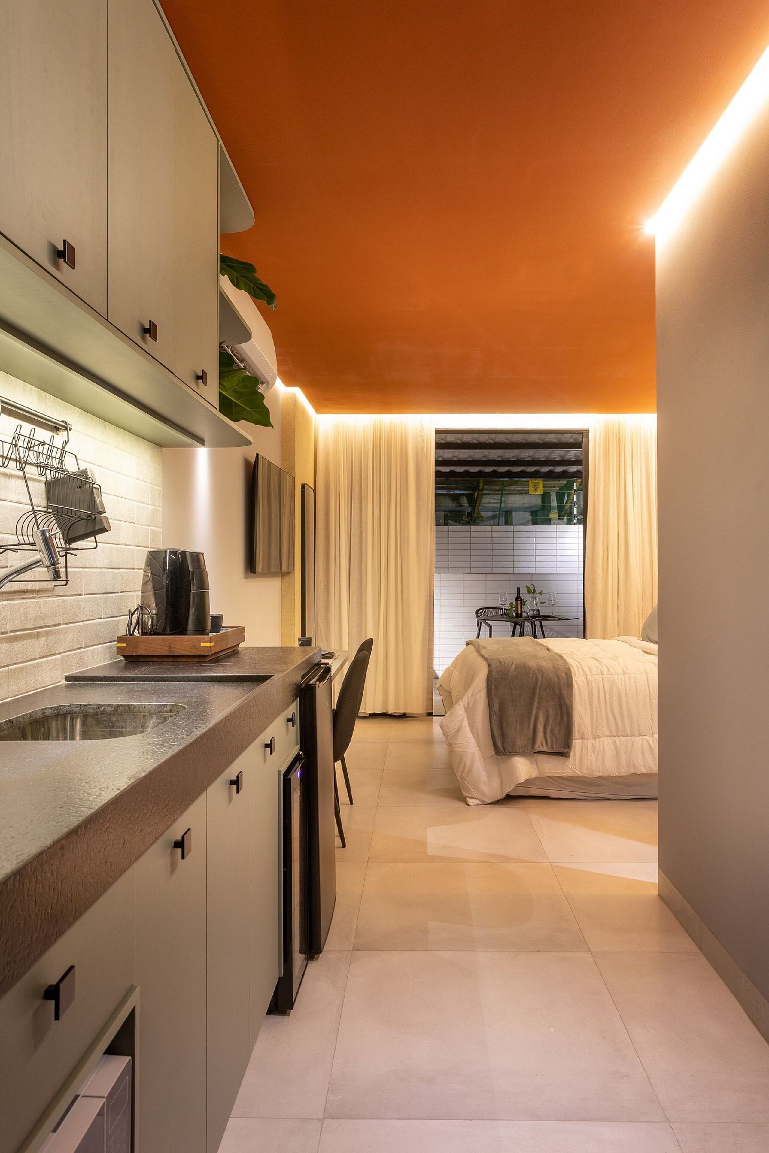 Quarto de hotel compacto com cozinha compacta, uma cama, área de refeições e janela com cortinas.