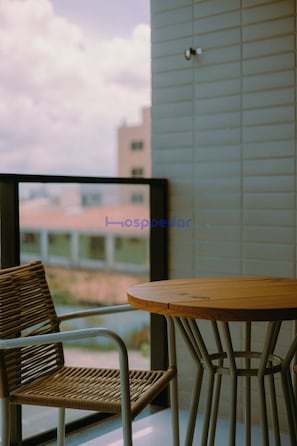 Un balcón con sillas de mimbre y una mesa redonda, una ventana con vistas a edificios y una pared con diseño de cuadrícula.