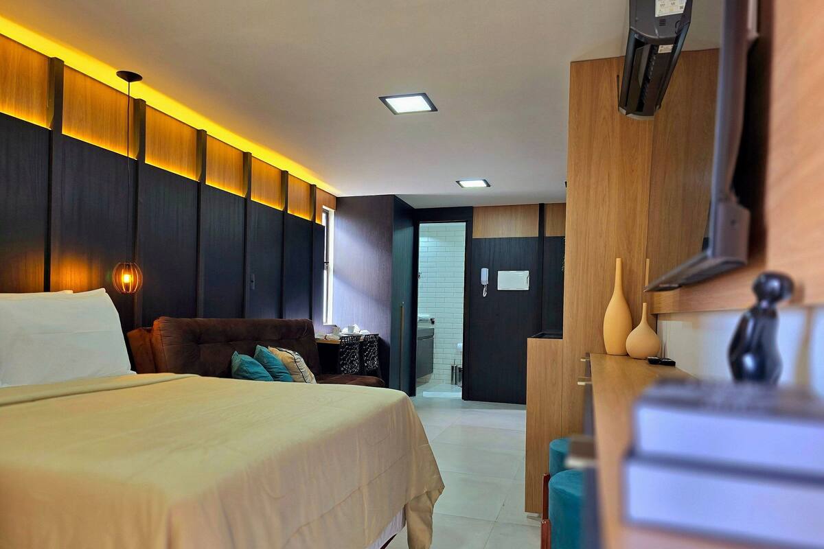 A hotel room with a bed, bedside table, lamp, and a view of the hallway.