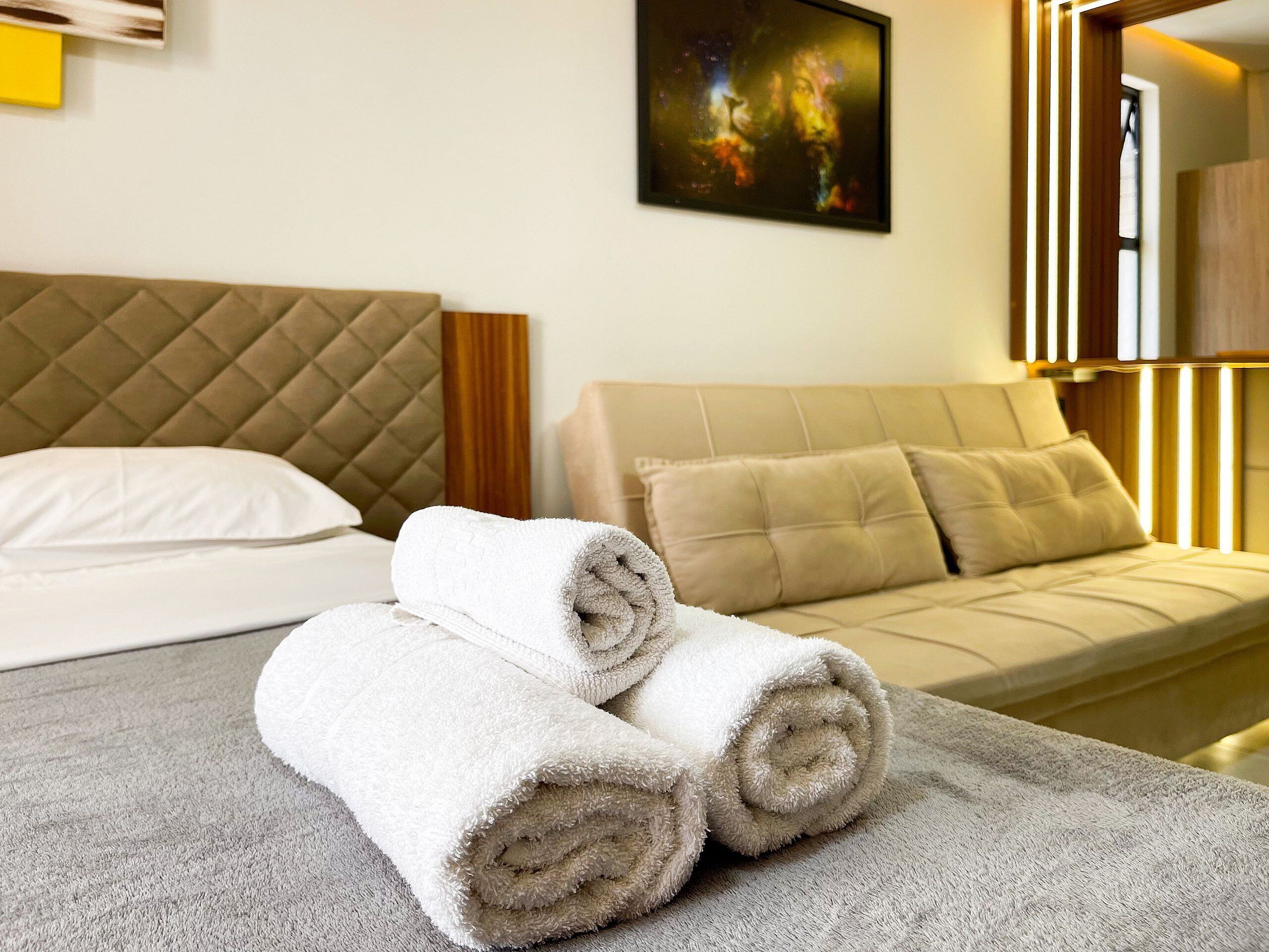 A hotel room with a bed, a sofa, and a painting on the wall.
