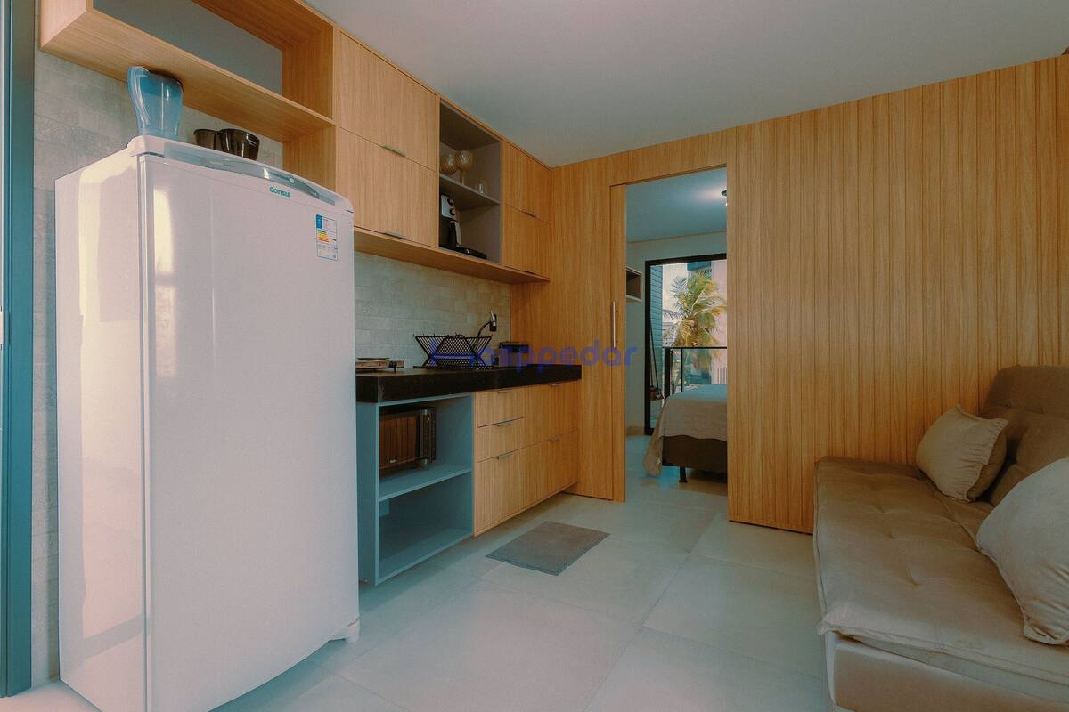 A compact kitchen with a refrigerator, wooden cabinets, and a sofa in a living area.