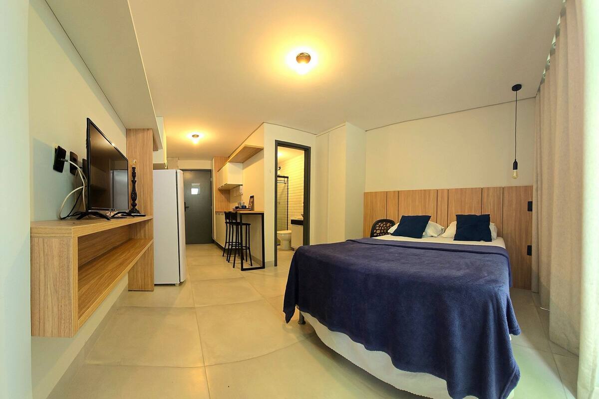 A hotel room with a bed, a TV, a desk, and a kitchenette.