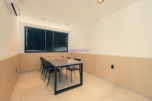 Une salle de conférence dotée d’une table à plateau de verre, de chaises, d’une fenêtre avec stores et d’un mur recouvert de panneaux en bois.