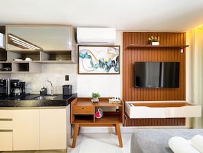 Una cocina compacta con cafetera, un lavamanos y un televisor de pantalla plana montado en una pared de madera.