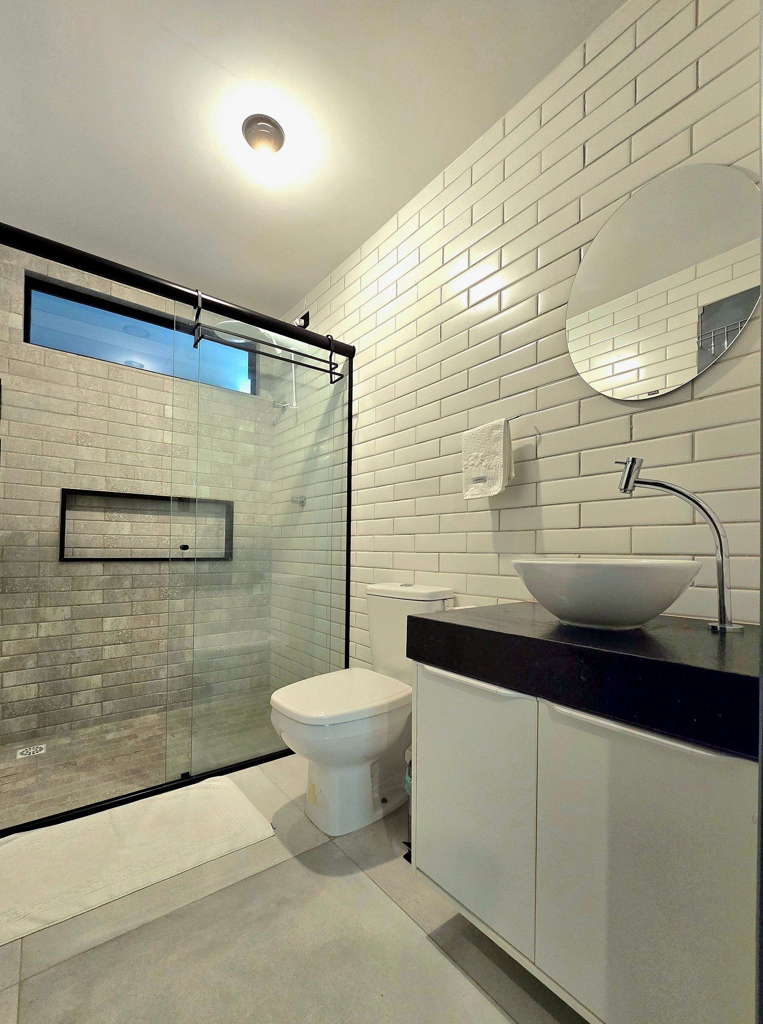 Un baño moderno con cabina de ducha de vidrio, inodoro blanco, lavabo de cuenca grande y espejo en la pared.