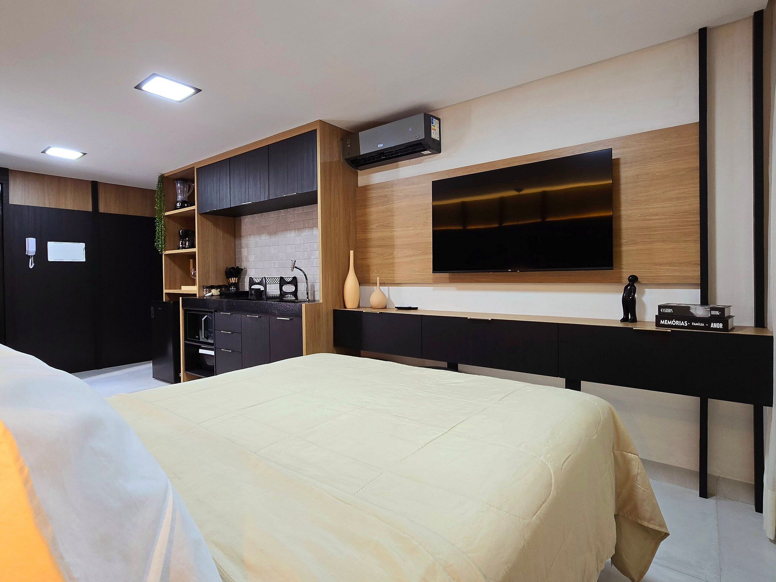 Un dormitorio moderno con cama, televisor montado en la pared, zona de cocina y teléfono en la pared.
