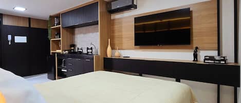 Une chambre moderne avec un lit, un téléviseur fixé au mur, un coin cuisine et un téléphone mural.