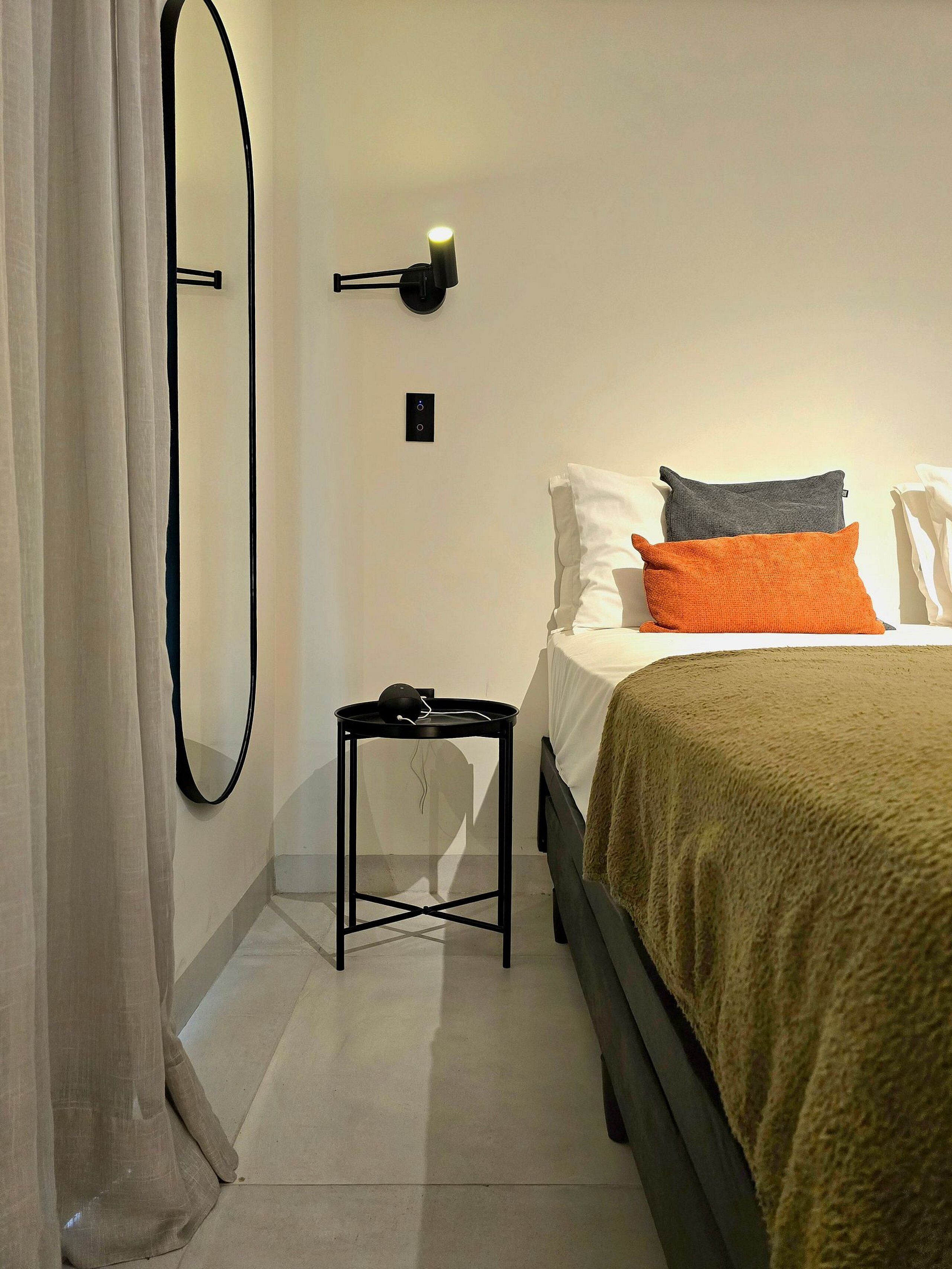 Un dormitorio con una cama, una mesita de noche, una lámpara de pared y un espejo.