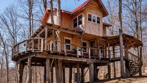 A wooden cabin with a deck and multiple levels, surrounded by trees. - 2BR, 1BA  HAND BUILT MOUNTAIN TOP TREE HOUSE with Hot tub (Nashville)
